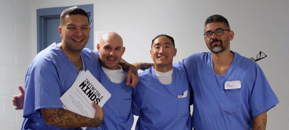 Four men with arms around eachother holding a draft of their book